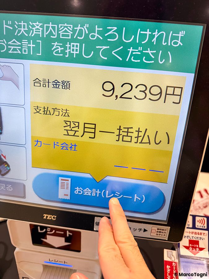 Dito di una persona che tocca lo schermo di una cassa automatica per confermare un pagamento in Giappone.