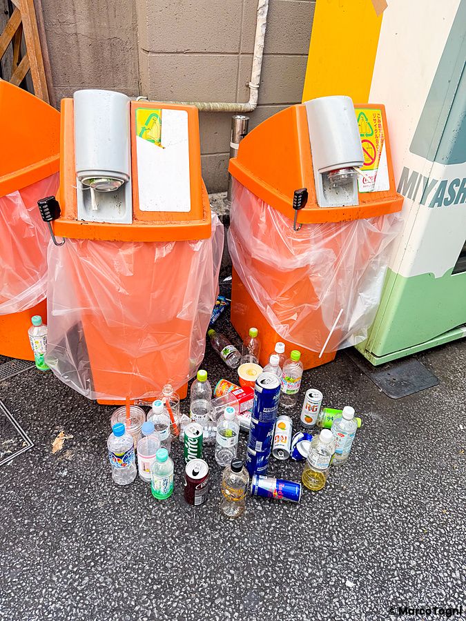 Cestino pieno di bottiglie e lattine accanto a un distributore automatico.