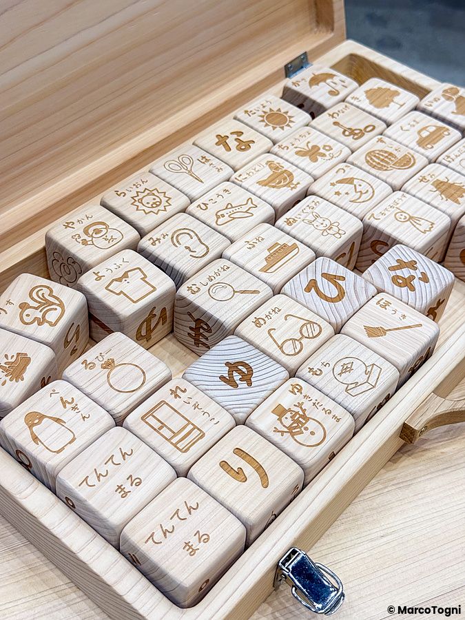 Cubi educativi in legno incisi con simboli e testo in hiragana all'interno di una scatola presso la Good Life Fair.