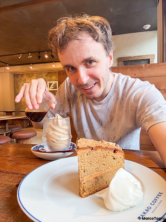 Marco Togni sorridente versa del caffè su un affogato al Takao Coffee, dove è presente anche una fetta di dolce nel piatto.