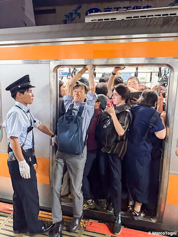 Un addetto in divisa assiste i passeggeri mentre salgono su un treno sovraffollato in stazione a Tokyo.
