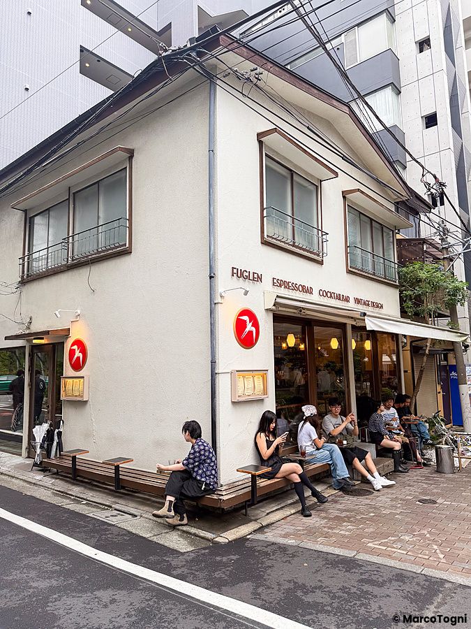 Esterno del caffè Fuglen vicino alla stazione Yoyogi-Hachiman a Tokyo con persone sedute sulle panchine lungo l'edificio.
