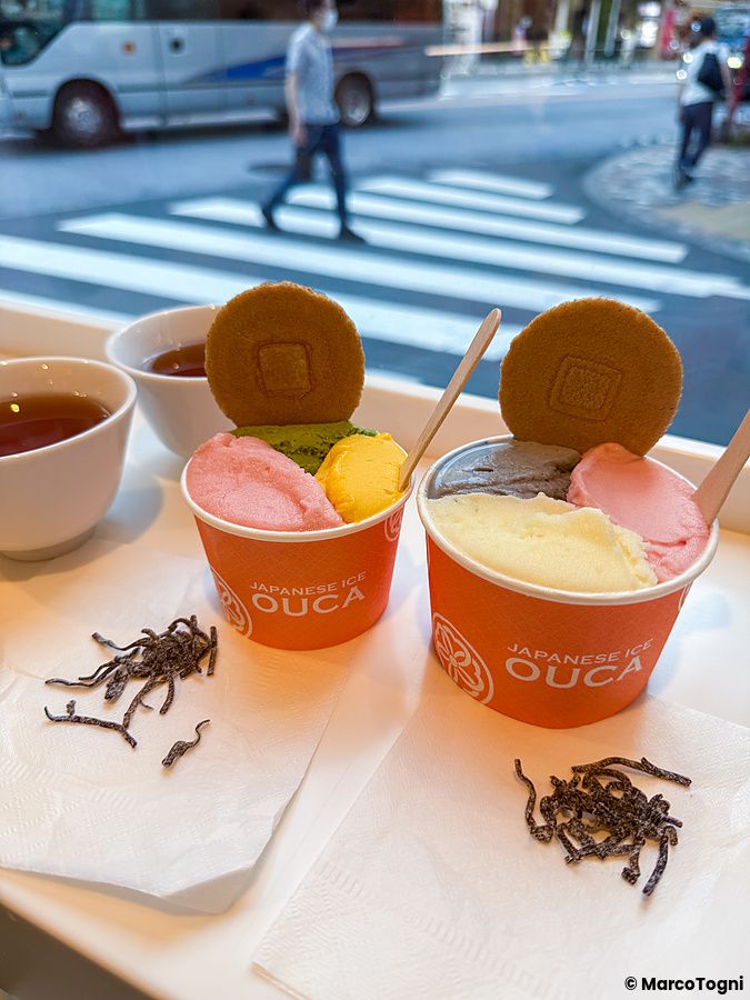 Due coppette di gelato con logo Ouca su un tavolo accanto a una vetrina che affaccia su una strada a Ebisu, Tokyo.