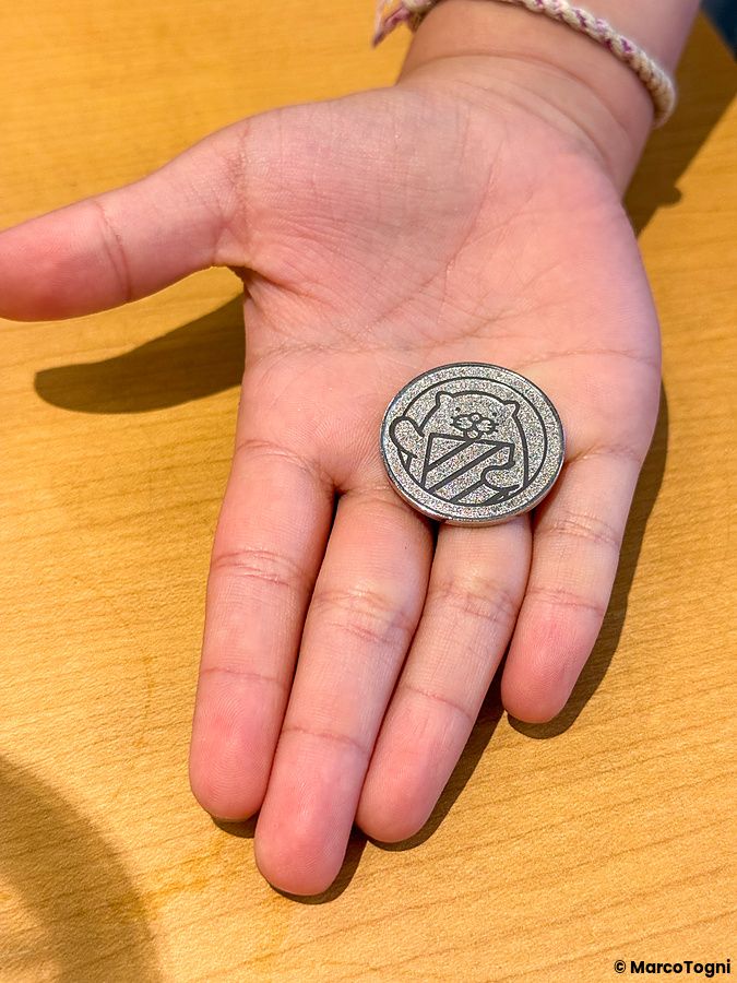 Una mano di un bambino tiene un gettone metallico circolare per vincere un premio presso il ristorante Sushiro.
