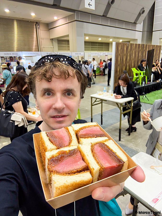 Marco Togni con sandwich vegano in mano a un evento a Tokyo.