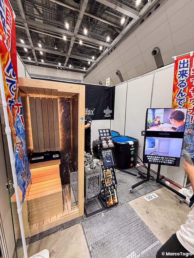 Uno stand della Good Life Fair a Tokyo con una sauna in legno, una vasca per immersione e schermi informativi.