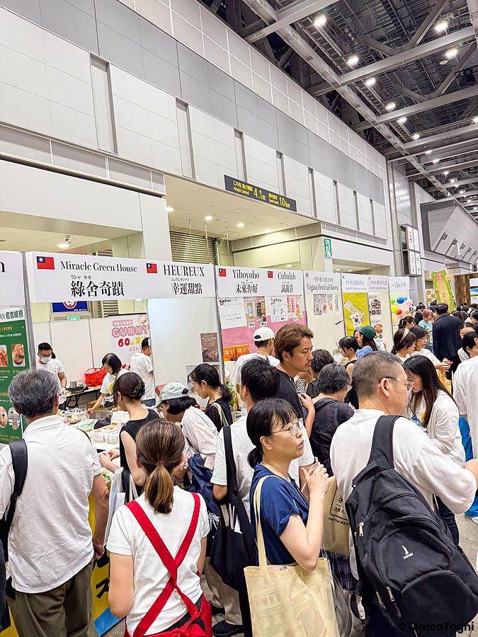 Una folla di persone visita gli stand della fiera Good Life Fair a Tokyo, esplorando proposte per uno stile di vita vegano.