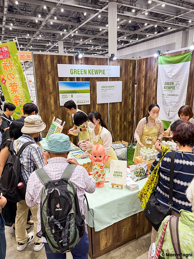 Uno stand espositivo di Green Kewpie alla Good Life Fair di Tokyo con addetti al banco che servono campioni ai visitatori.