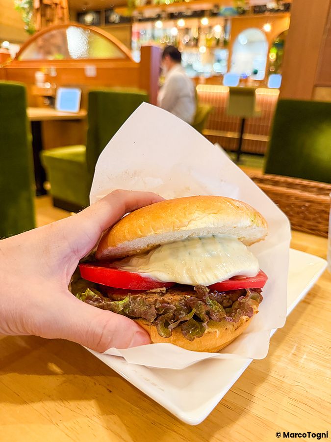 Una mano tiene un hamburger vegano farcito con pomodoro e lattuga servito nel ristorante Komeda Is a Ginza.