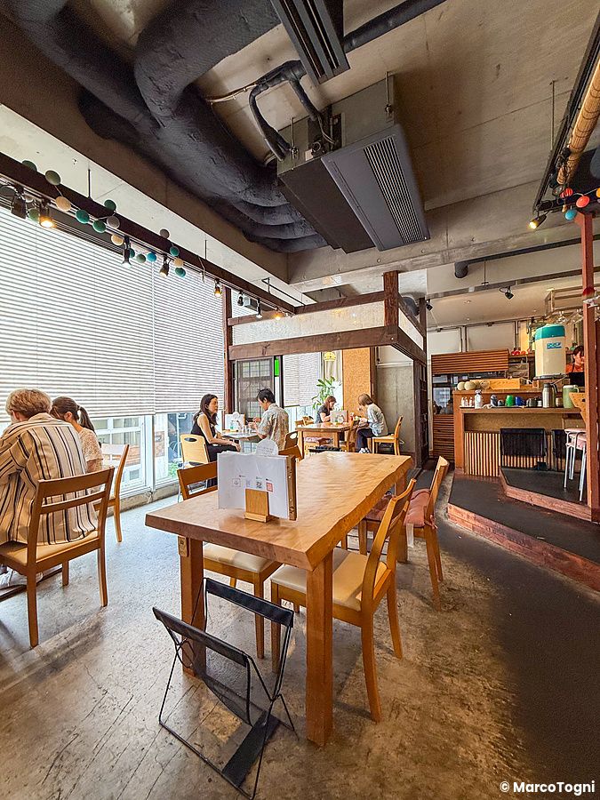 Interno del locale Kanna a Setagaya con tavoli in legno, pavimento in cemento e alcune persone sedute a mangiare.