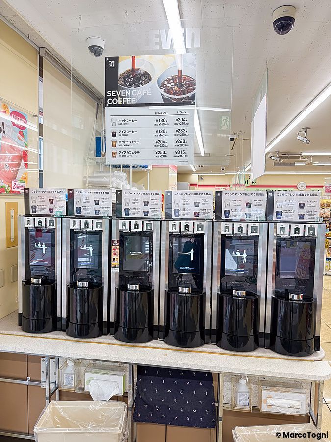 Macchinette per il caffè al 7 Eleven allineate su un bancone con menu sopra.
