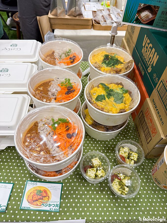 Piatti pronti vegani in ciotole trasparenti esposti su una tovaglia a pois verdi alla Good Life Fair di Tokyo.