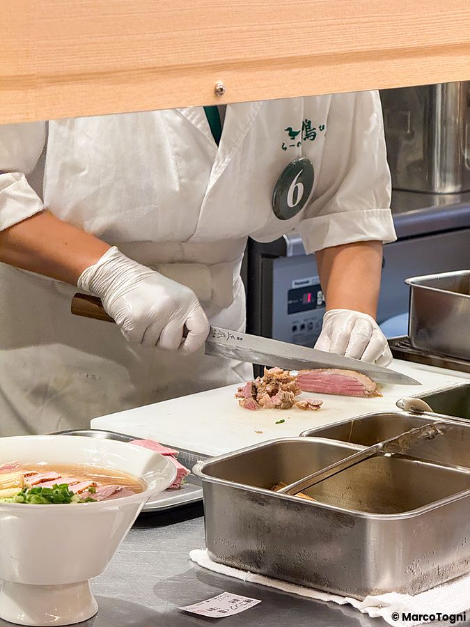 Un cuoco con divisa bianca prepara carne d'anatra su un tagliere all'interno del ristorante Ramen Kamo to Negi.
