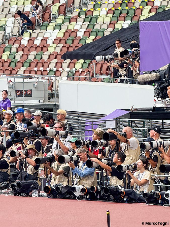 Un gruppo di fotografi con teleobiettivi all'interno dello Stadio Nazionale Giapponese a Tokyo durante un evento sportivo.