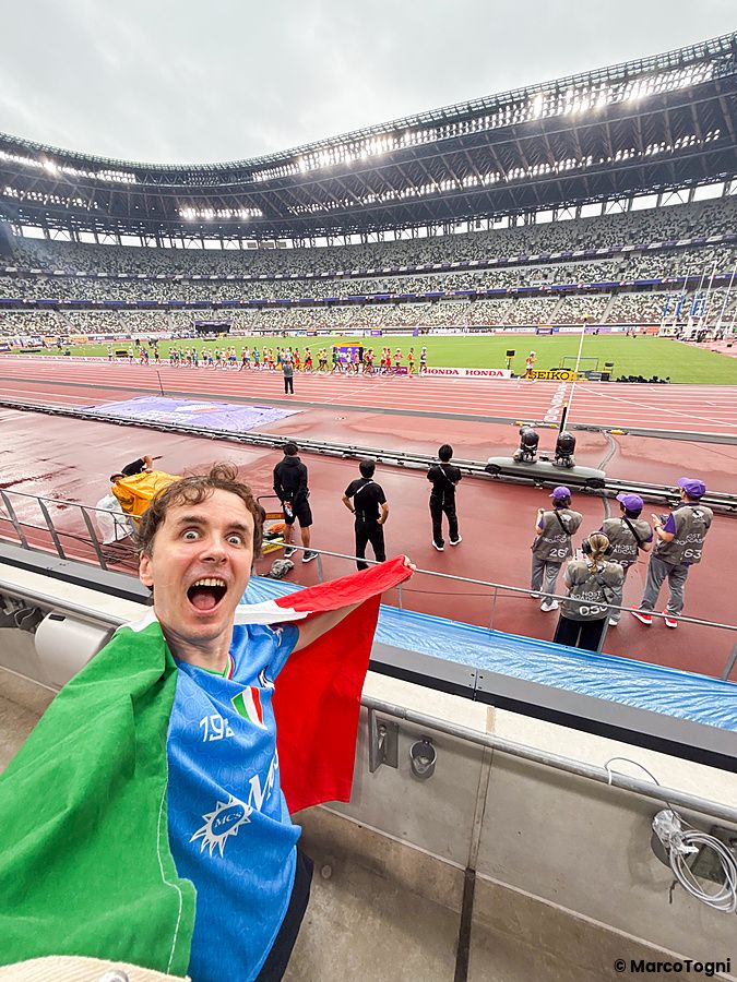 Marco Togni con una bandiera italiana fa un selfie all'interno allo Stadio Nazionale Giapponese a Tokyo durante una gara.