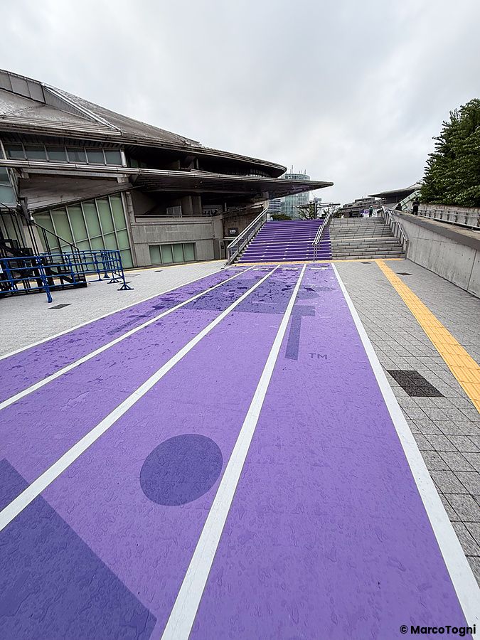 Veduta esterna dello Stadio Nazionale Giapponese a Tokyo con una pista di atletica viola disegnata sul suolo.
