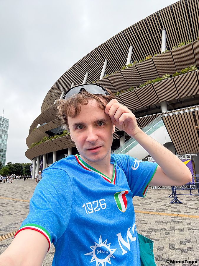 Marco Togni in maglia azzurra scatta un selfie all'esterno dello Stadio Nazionale Giapponese a Tokyo, davanti alla struttura.
