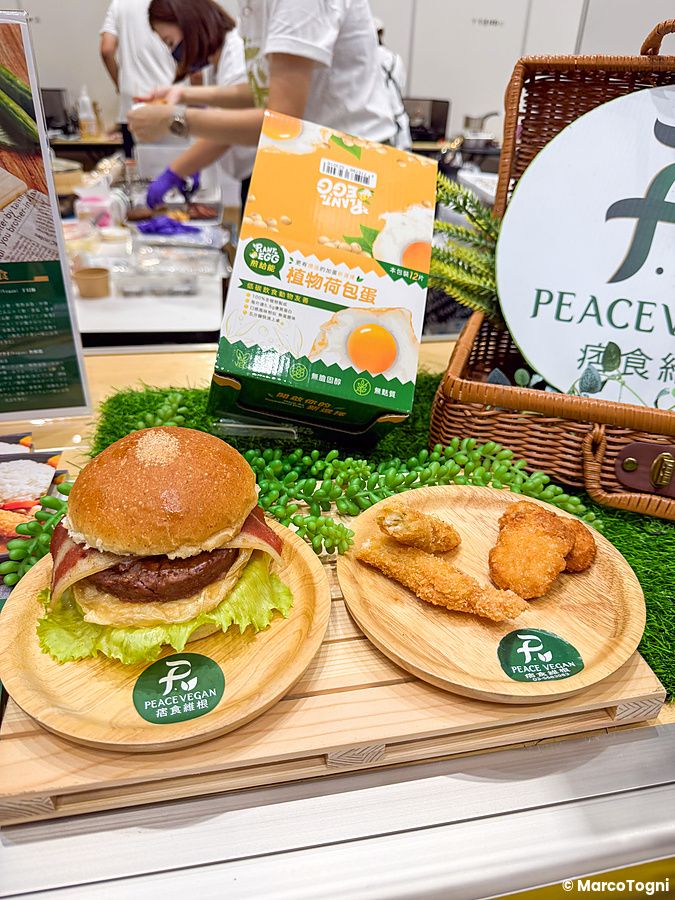 Hamburger vegano e crocchette vegetali esposti su piatti di legno alla Good Life Fair di Tokyo.