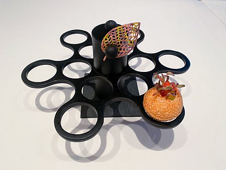 Una foglia cracker fissata da una calamita e una palla fritta con avocado su un supporto nero al Koji Shimomura.