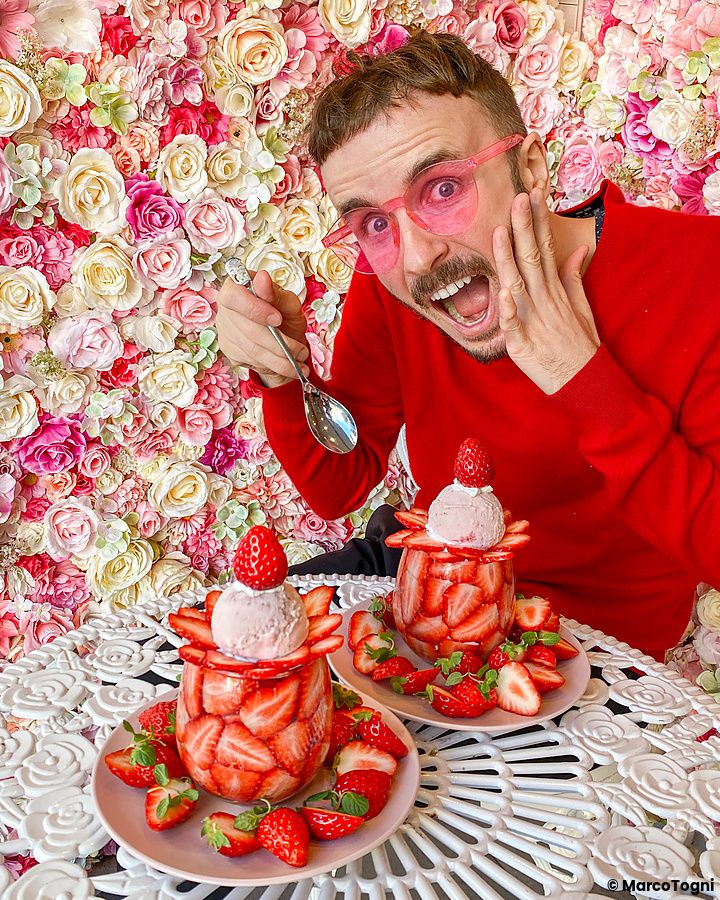 Marco Togni con dessert fragole e gelato davanti a parete floreale
