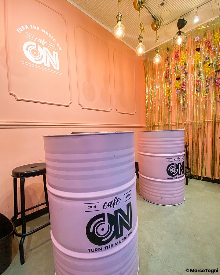 Interno di Cafe ON (Shin-Okubo, Tokyo) con tavoli a forma di bidone rosa e decorazioni floreali sulla parete.