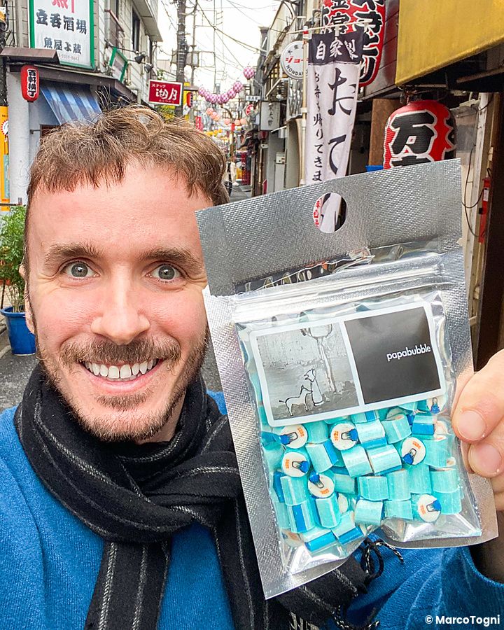 Marco Togni sorride tenendo un sacchetto di caramelle artigianali a Papabubble in una strada di Tokyo.