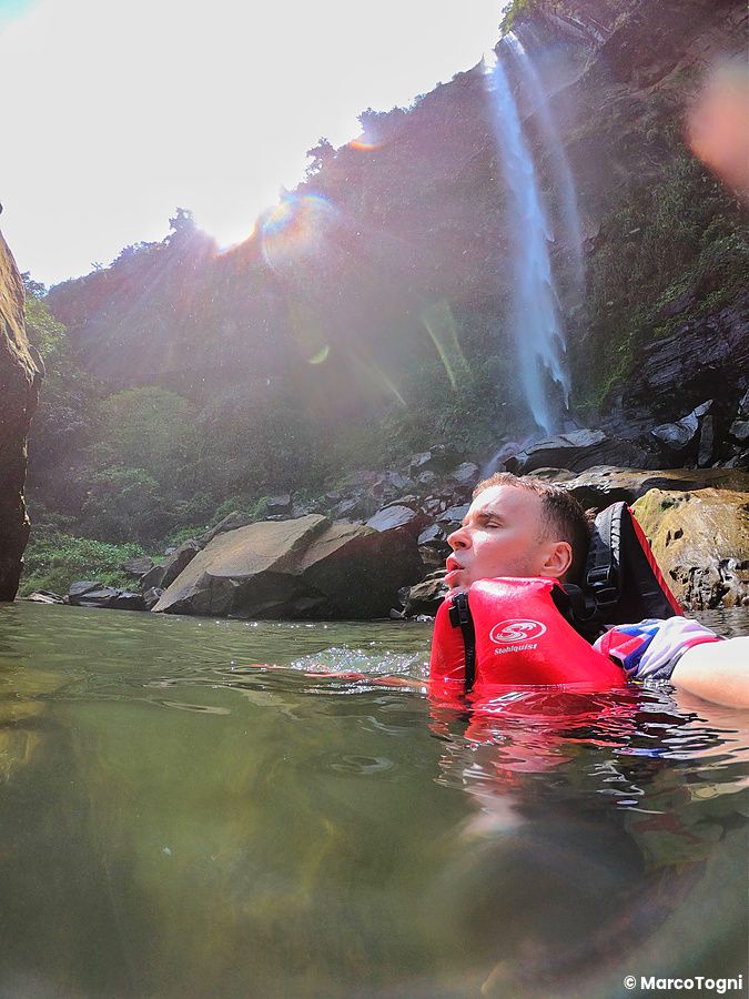 Marco Togni con giubbotto di salvataggio rosso nuota nelle acque delle cascate Pinsaira.