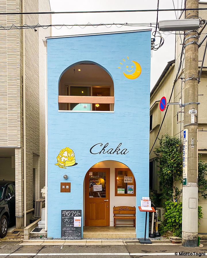 La facciata azzurra della sede di Chaka a Tokyo con un ingresso ad arco e una luna sorridente disegnata sul muro.