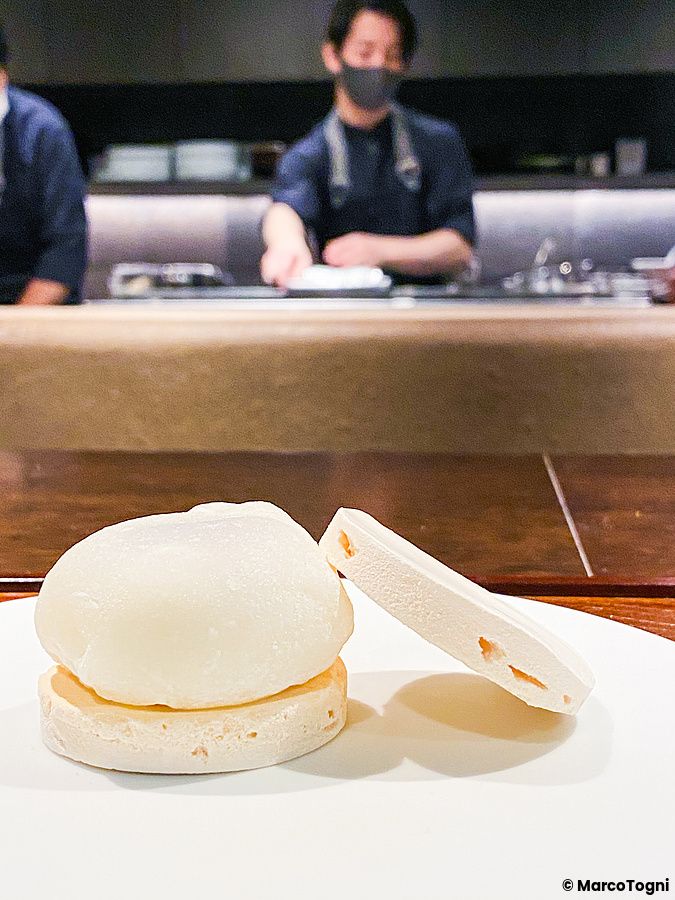 Un daifuku freddo con crema tra due meringhe su un piatto al ristorante Denkushiflori, con una persona sullo sfondo.