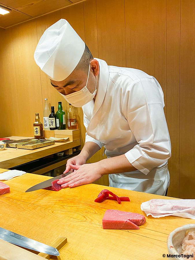 Uno chef indossa una divisa bianca e una mascherina mentre esegue il taglio del maguro a Ginza Iwa.