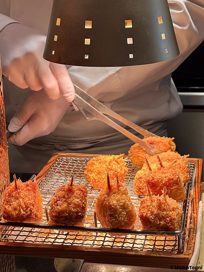 Chef che utilizza delle pinze per maneggiare pezzi di tonkatsu fritto su una griglia al Ginza Katsukami di Tokyo.