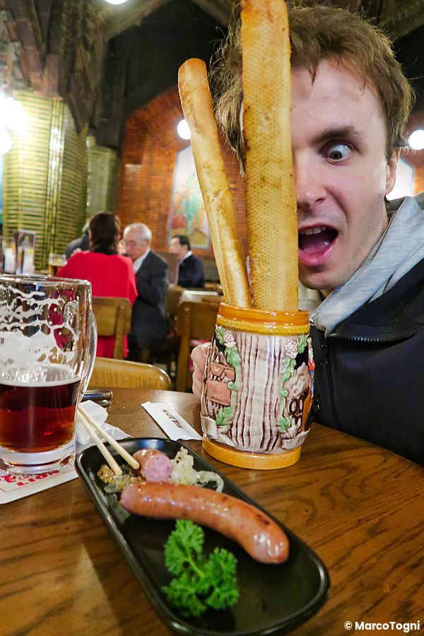 Marco Togni scherza con un boccale di pane da Ginza Lion a Tokyo, con birra e salsicce sul tavolo in primo piano.