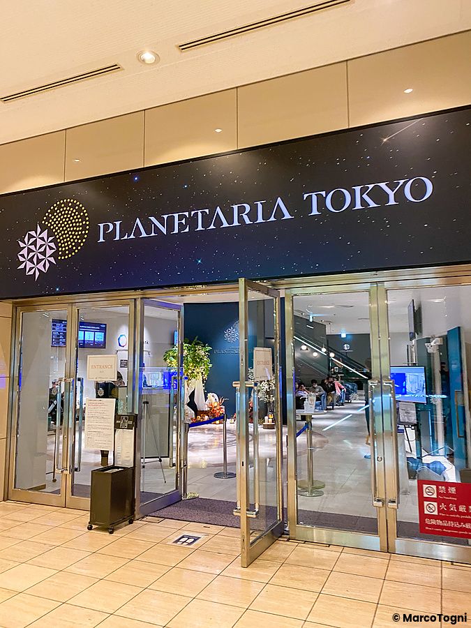 L'ingresso in vetro con porte a battente del Planetaria Tokyo, caratterizzato da un'insegna scura con scritte bianche.