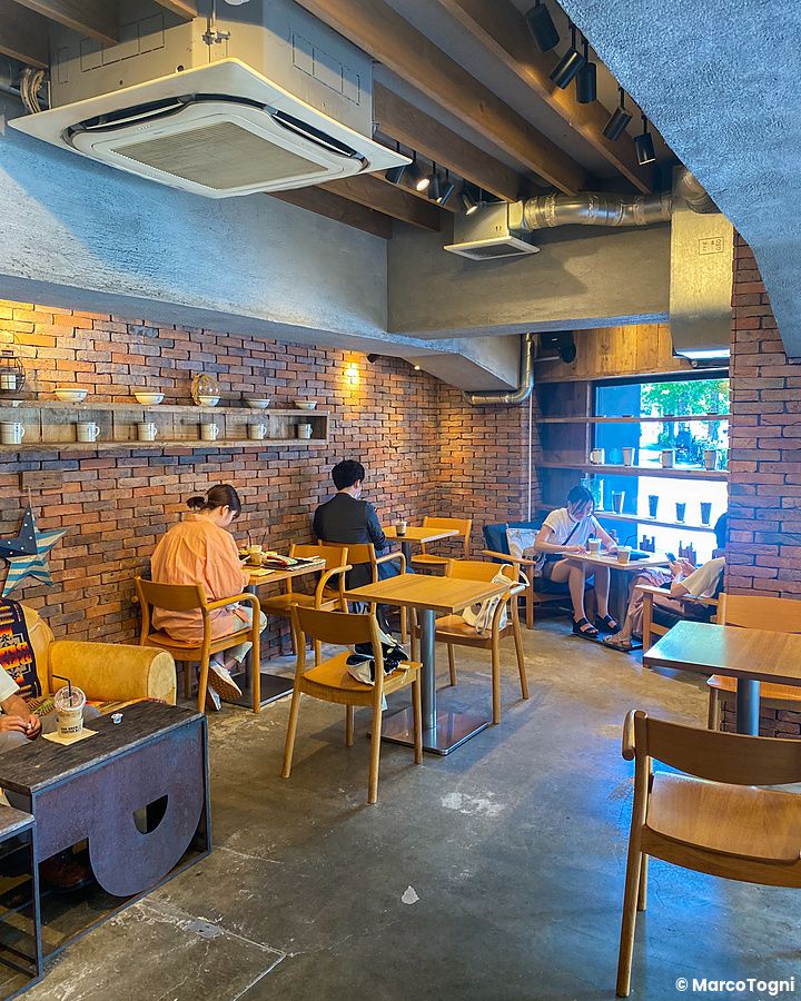 Veduta degli interni in mattoni del caffè The Deck Coffee & Pie a Tokyo con persone sedute ai tavoli in legno.
