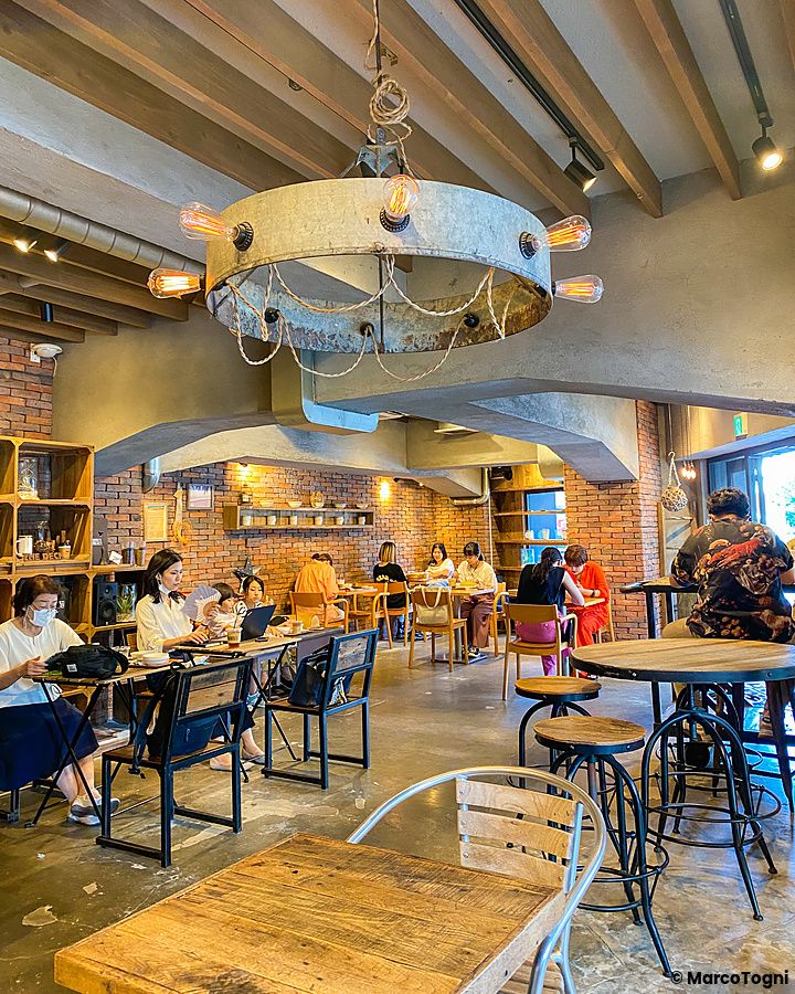 Interno del locale The Deck Coffee & Pie a Tokyo con clienti seduti ai tavoli tra arredi in mattoni e legno.