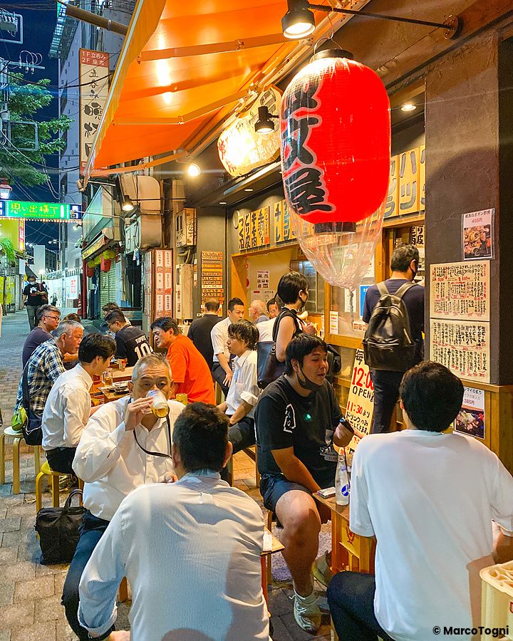 Persone sedute fuori in un izakaya a Tokyo con lanterne rosse.