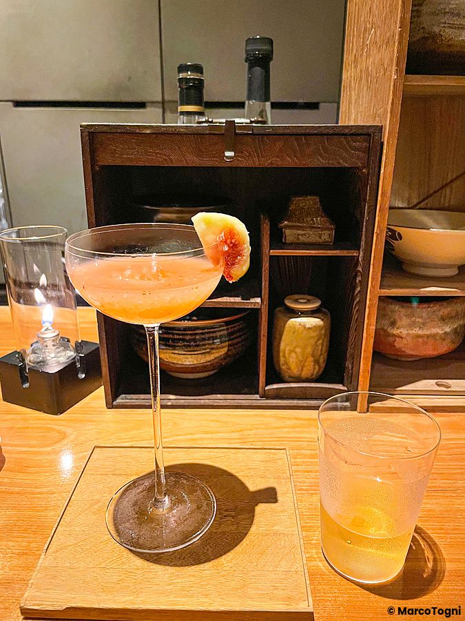 Un cocktail rosato con guarnizione di fico fresco su un bancone di legno presso il Mixology Salon a Ginza, Tokyo.