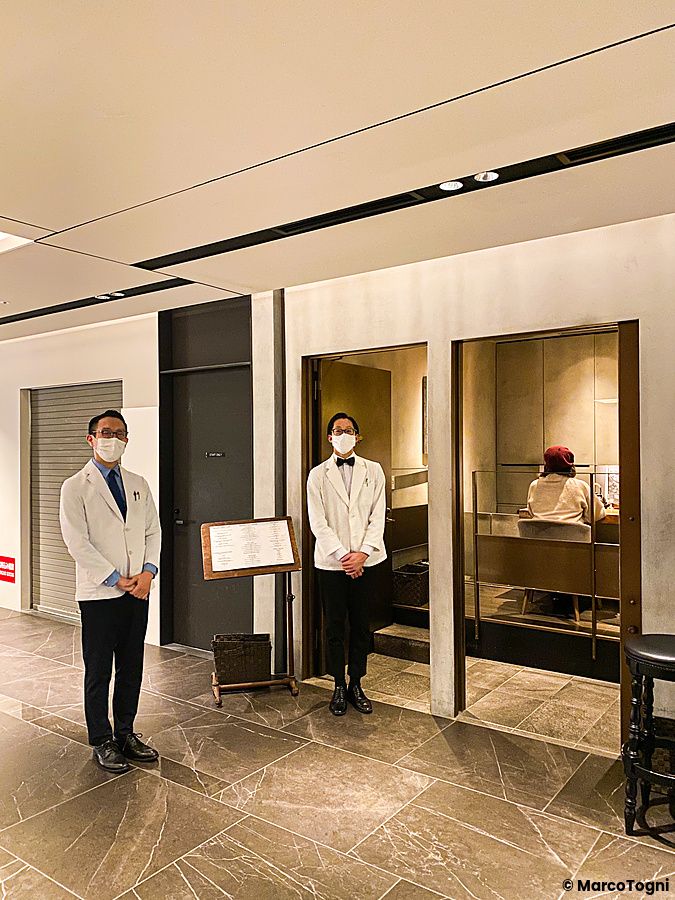 Due uomini in uniforme bianca accolgono i visitatori all'ingresso del Mixology Salon nel quartiere Ginza a Tokyo.