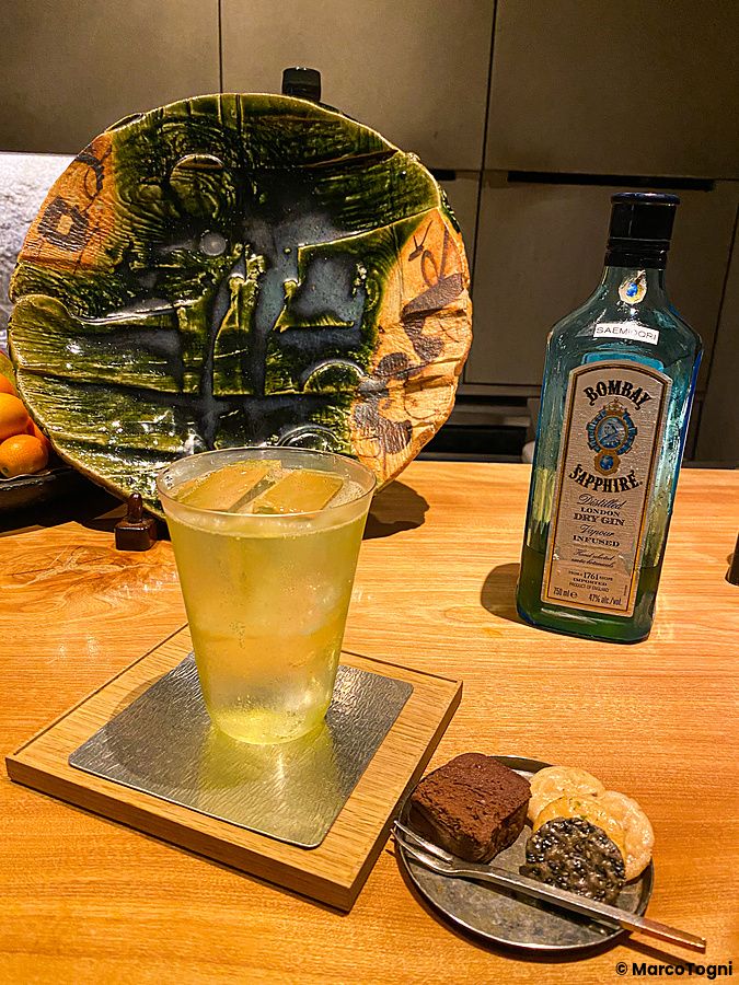 Un cocktail e una bottiglia di Bombay Sapphire sono appoggiati su un bancone di legno al Mixology Salon di Ginza, Tokyo.