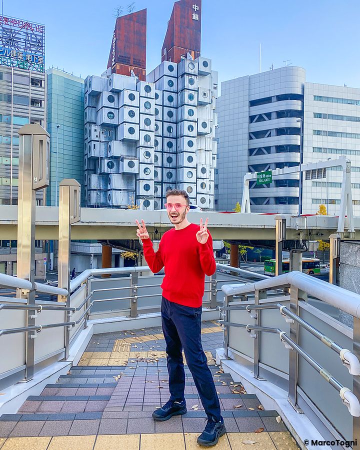Una persona davanti alla Nakagin Capsule Tower a Tokyo mostrando il segno di pace.