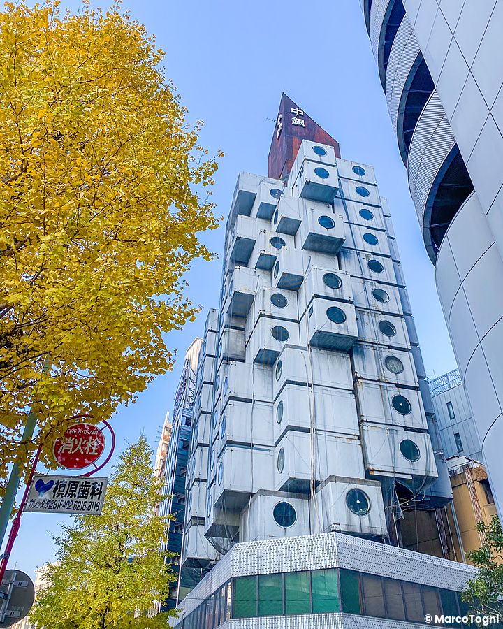 Nakagin Capsule Tower a Tokyo con cielo azzurro e foglie dorate.