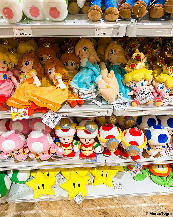 Scaffali del Nintendo Store a Tokyo pieni di peluche dei personaggi di Super Mario come Peach, Toad e stelle gialle.