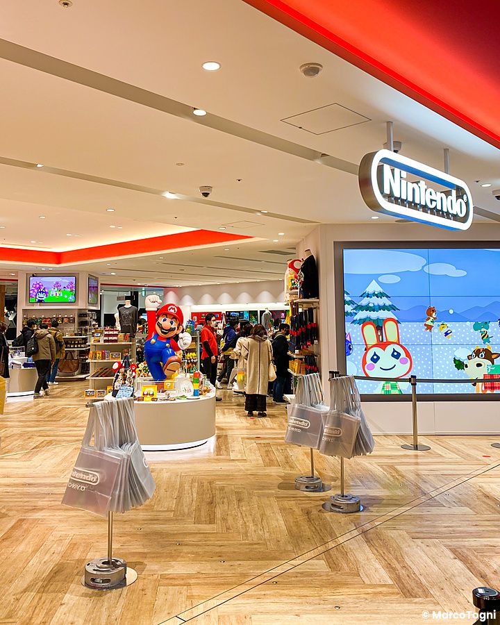 Interno del Nintendo Store al Shibuya Parco con una statua di Mario al centro e clienti tra gli scaffali di prodotti.