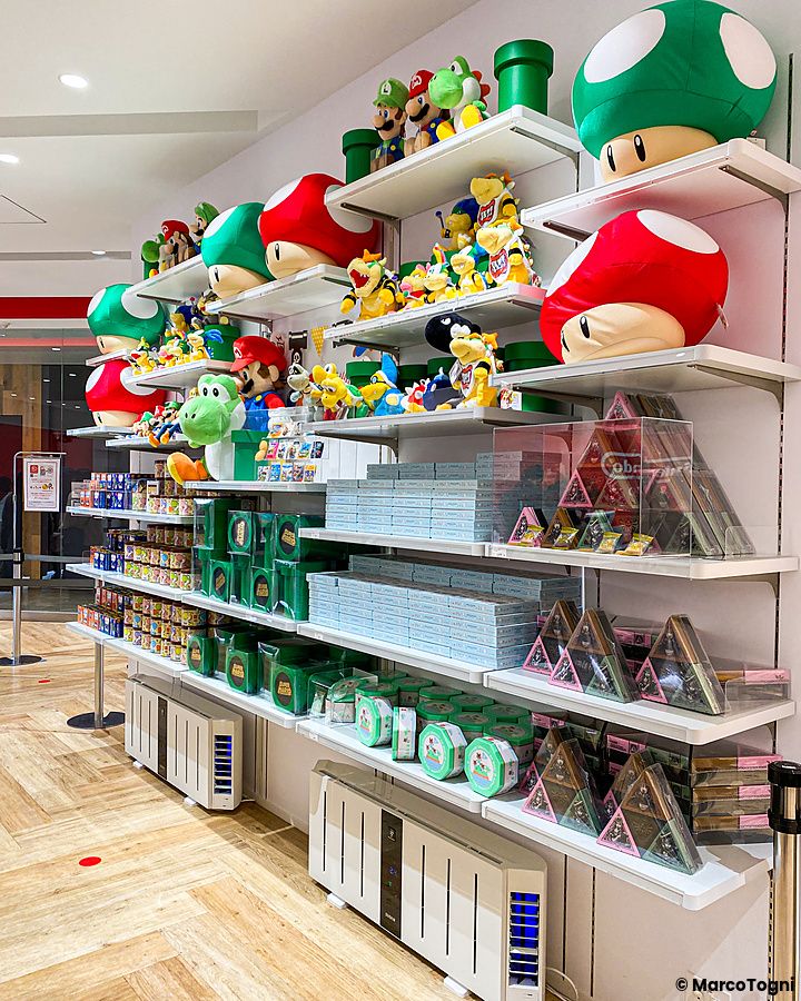 Scaffali bianchi del Nintendo Store a Tokyo pieni di peluche di Mario, Yoshi e vari gadget a tema videoludico.
