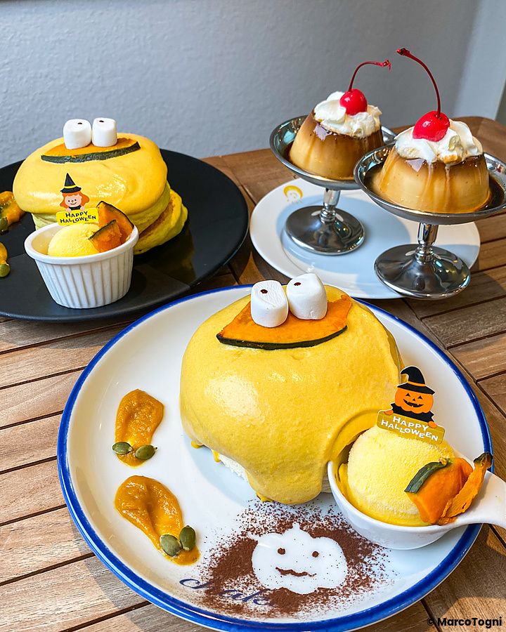 Due piatti con pancake alla zucca a tema Halloween decorati con occhi di marshmallow e una coppetta di budino.
