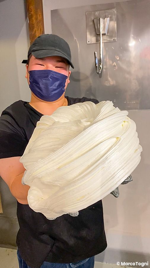 Una persona con mascherina blu mostra una grande massa di zucchero bianco durante la preparazione caramelle a Papabubble.
