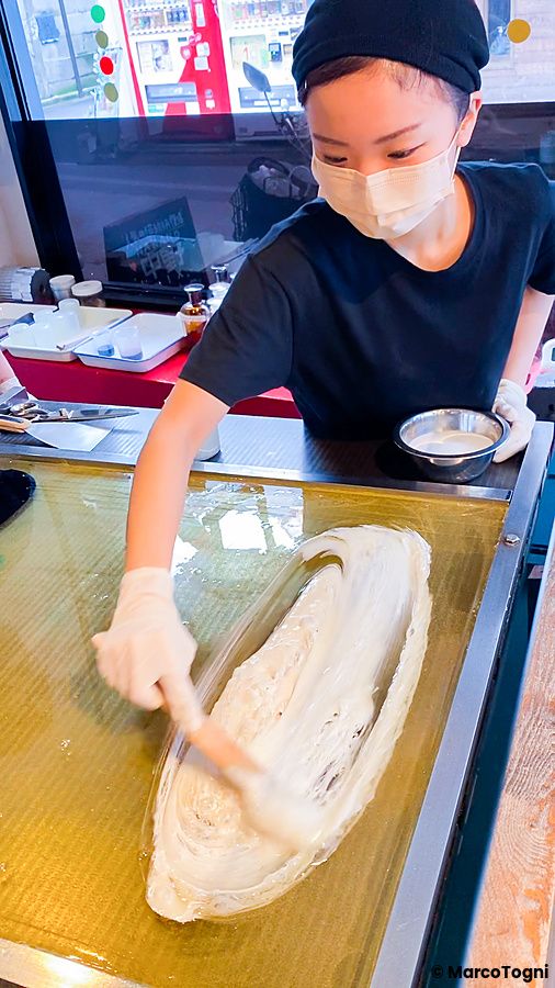 Una persona con guanti e mascherina lavora lo zucchero sul piano di cottura per la preparazione caramelle a Papabubble.