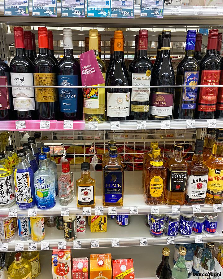Scaffali di un negozio conbini in Giappone pieni di bottiglie di vino, whisky e lattine di bevande alcoliche.