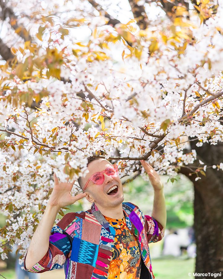 Marco Togni sorridente sotto un albero di ciliegio in fiore a Tokyo.