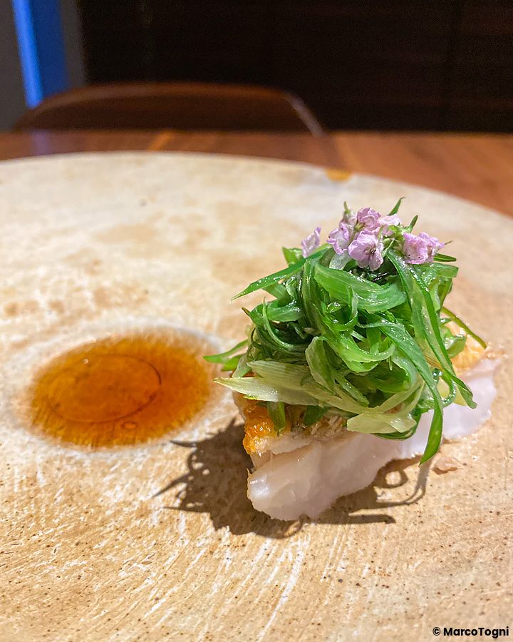 Pesce amadai con verdure, fiori di shiso e salsa di pesce servito in un piatto di ceramica al ristorante Le Sputnik.